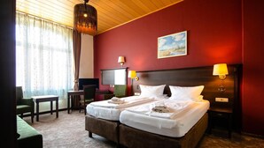 Een tweepersoonsbed met witte lakens, een bureau, een stoel en een televisie in een kamer met rode muren en een houten plafond.