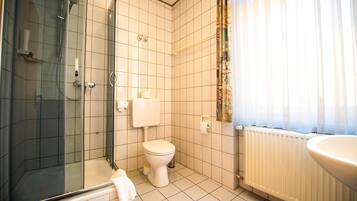 A bathroom with a glass-enclosed shower, a toilet, and a sink.