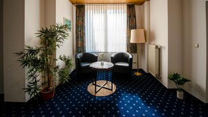 Hotelkamer met een houten plafond, een grote potbamoe, twee zwarte leren fauteuils, een klein rond tafeltje met een vaas, een vloerlamp en een radiator.