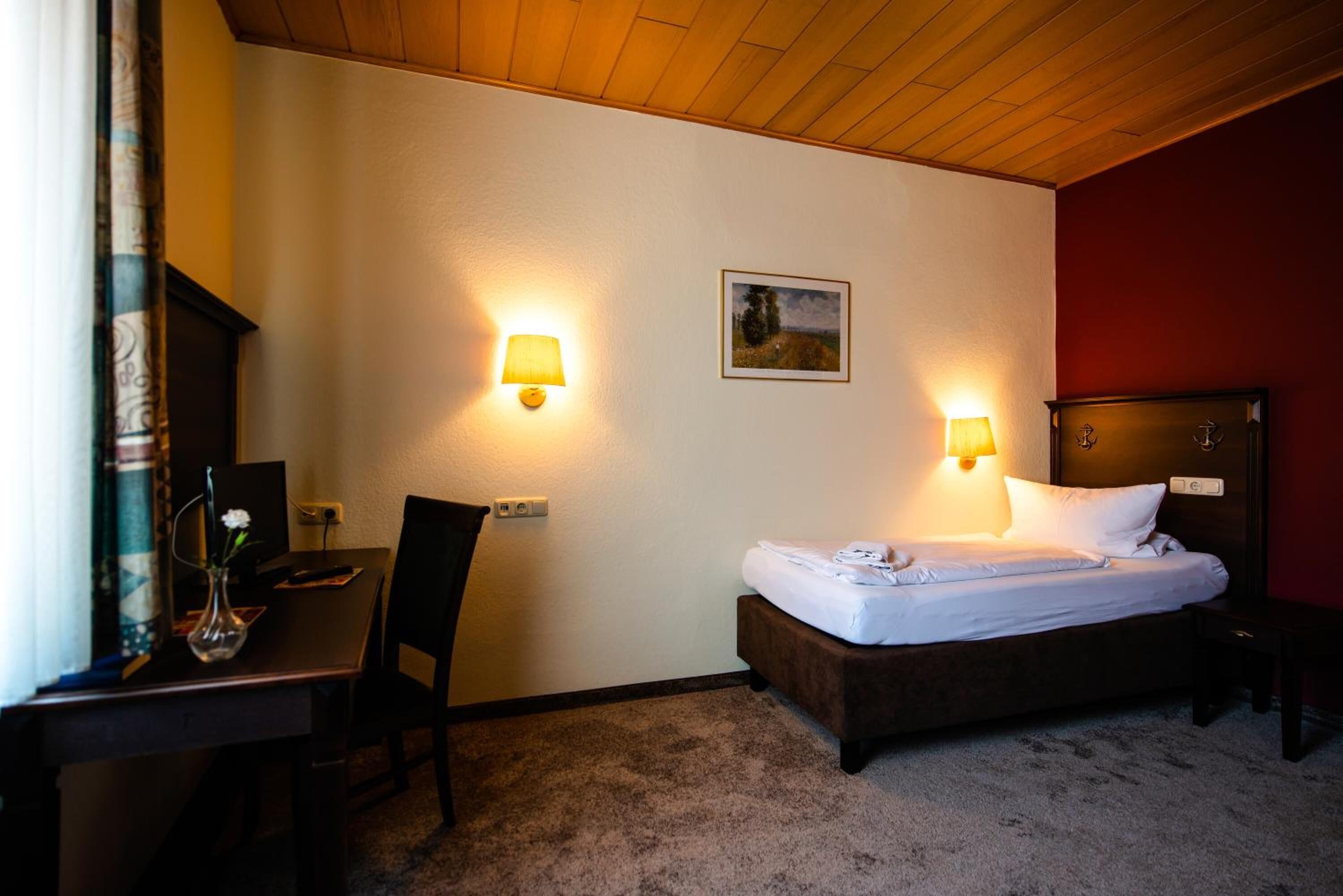 A hotel room with a bed, desk, chair, and two wall-mounted lamps.