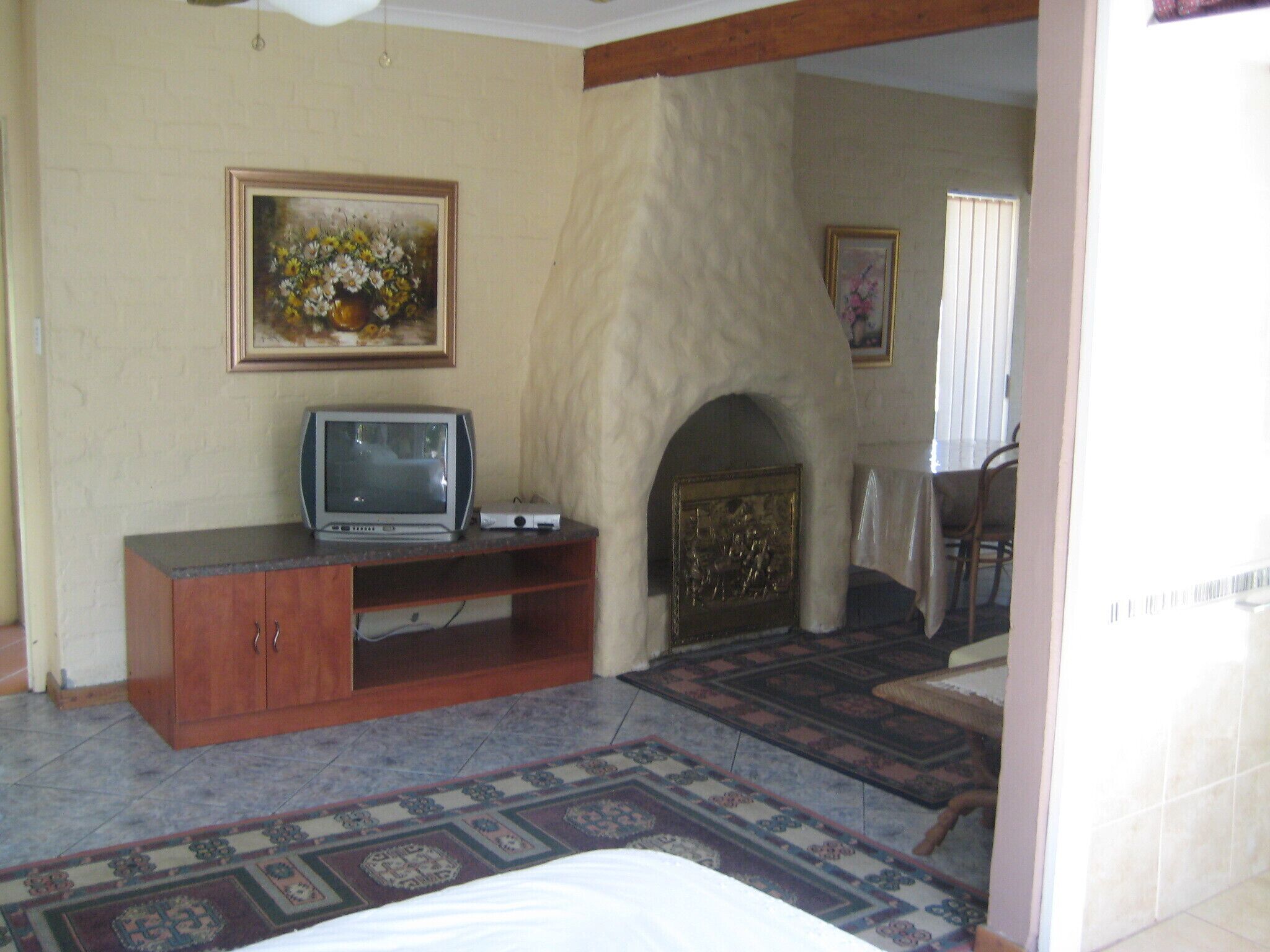 A room with a fireplace, a television on a wooden stand, a patterned rug, and a painting on the wall.