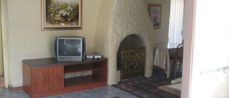 A room with a fireplace, a television on a wooden stand, a patterned rug, and a painting on the wall.