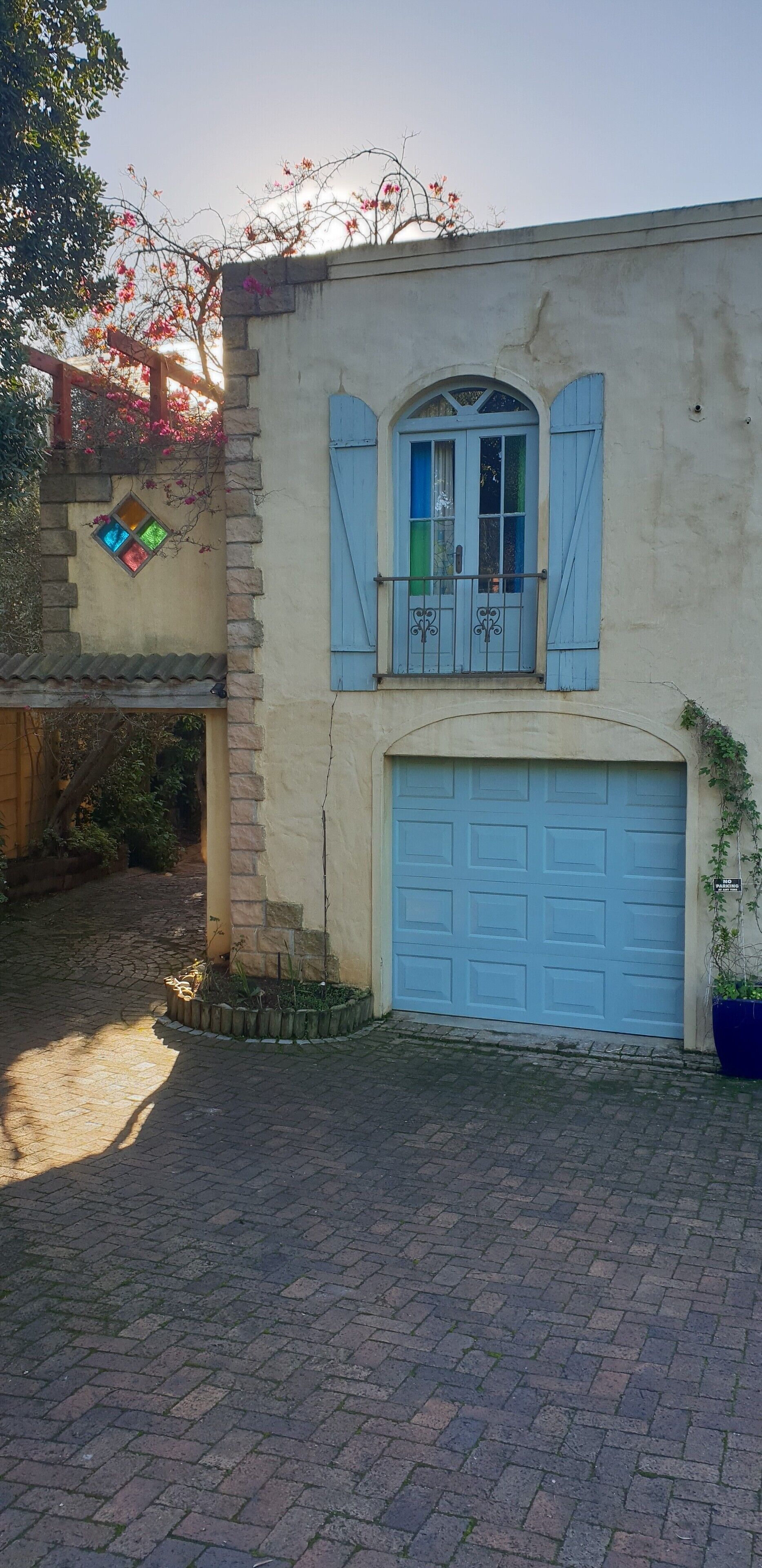 A building with a blue garage door, a small balcony with blue shutters, and a window with a colorful stained glass design.