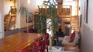 Uma área de refeições com uma mesa de madeira e cadeiras vermelhas, uma escada e uma planta grande.