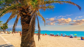 Ein Strand mit Palmen, badenden Personen und Sonnenschirmen.