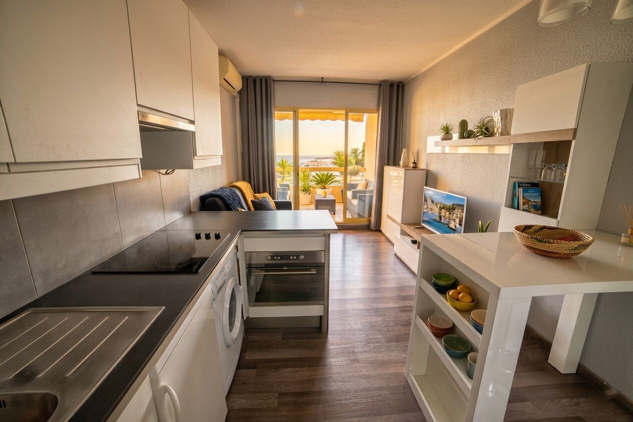 Cocina compacta con horno empotrado, lavadora y comedor con vistas.