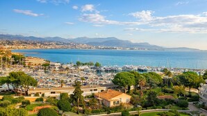 A marina with boats, a coastal town, and mountains in the background. - F2 luxury air-conditioned sea view 100 meters from the beach in the famous Marina. (Villeneuve-Loubet)