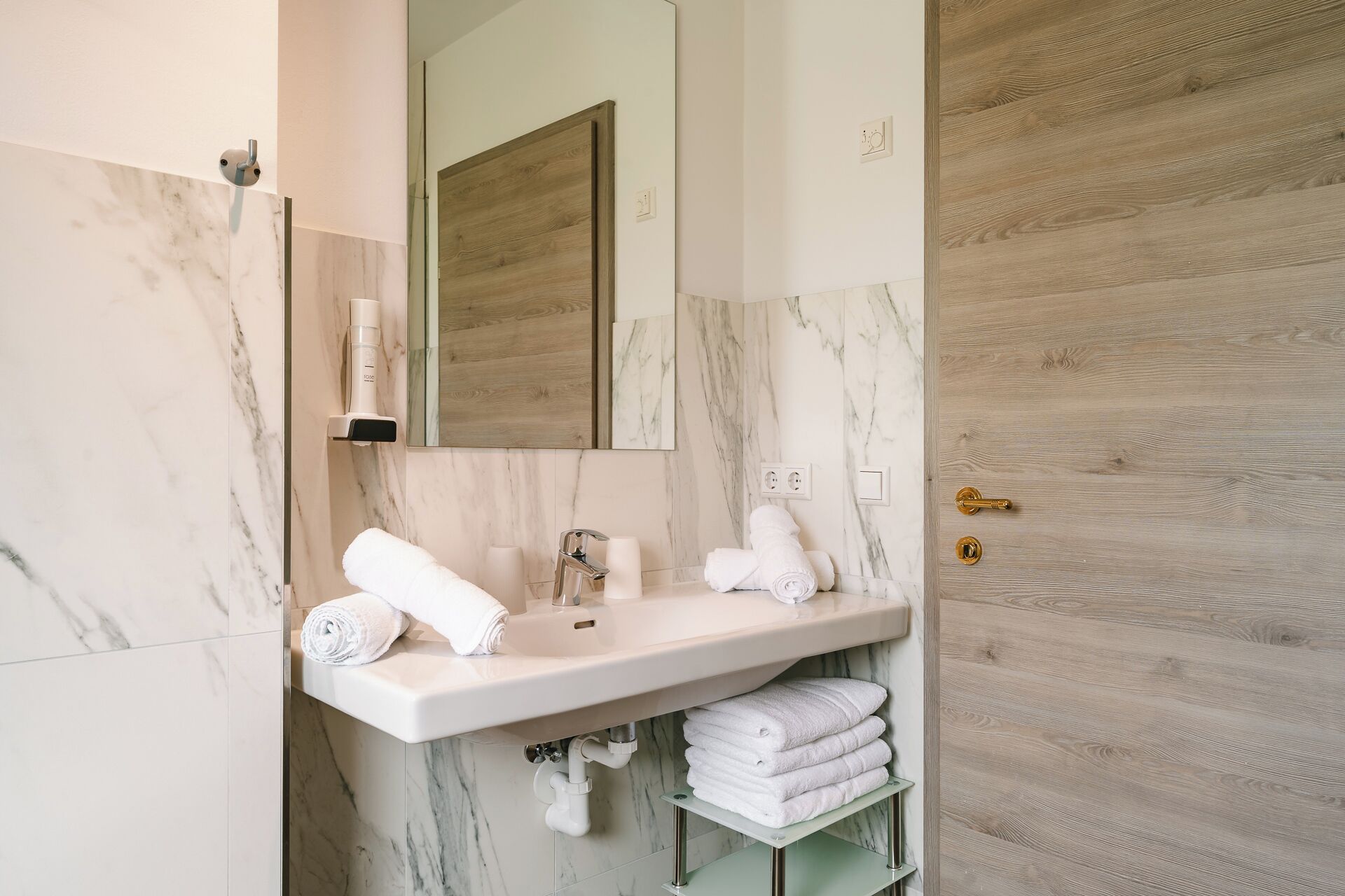 Une salle de bain avec un meuble-lavabo en marbre, un miroir, un porte-serviettes et une porte en bois.