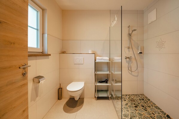 Un baño con inodoro, ducha y estante con toallas.