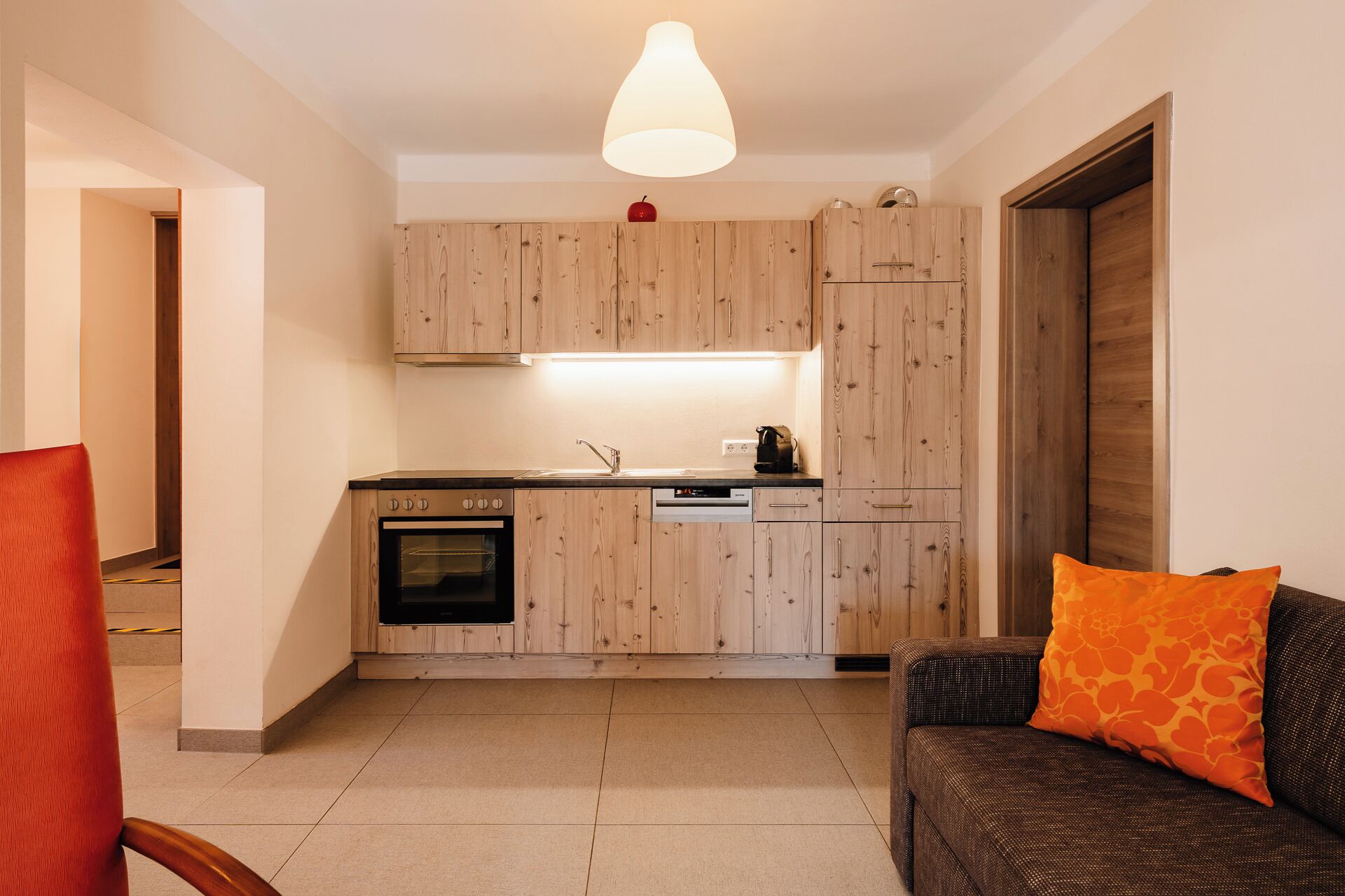 A compact kitchen with wooden cabinets, a built-in oven, and a coffee machine.