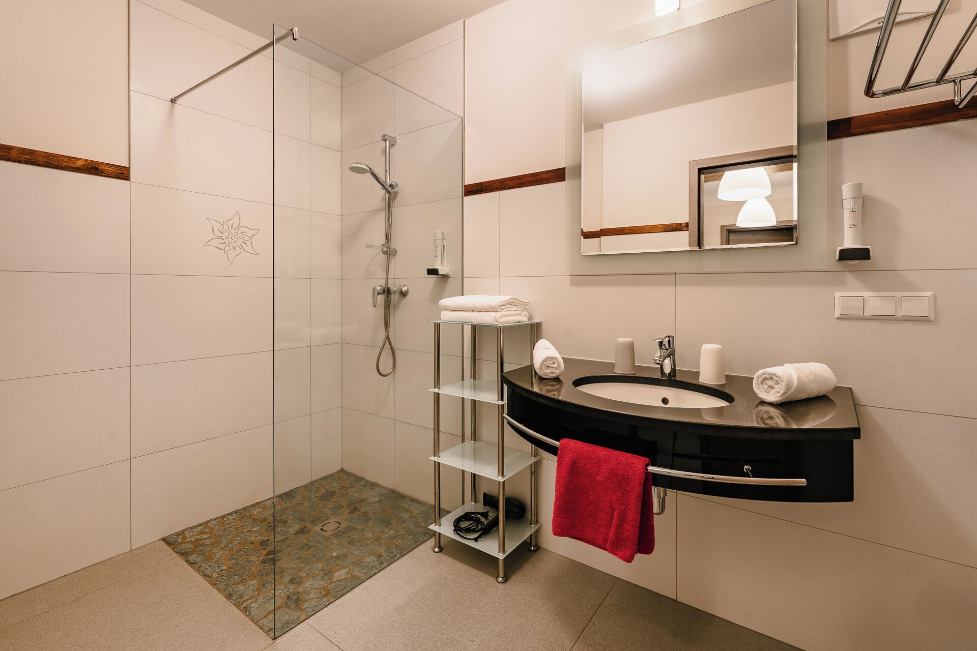 A modern bathroom with a glass shower enclosure, a vanity with a black countertop, and a mirror above the sink.