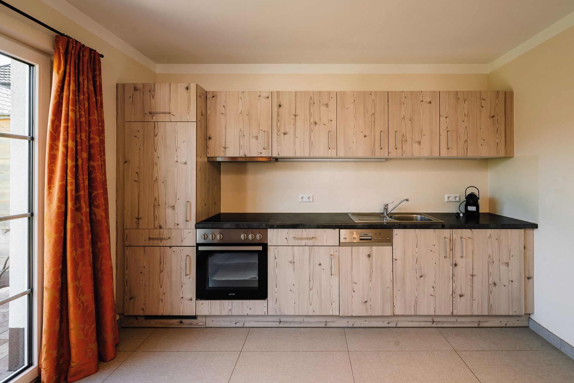 A modern kitchen with wooden cabinets, a built-in oven, a sink, and a kettle.