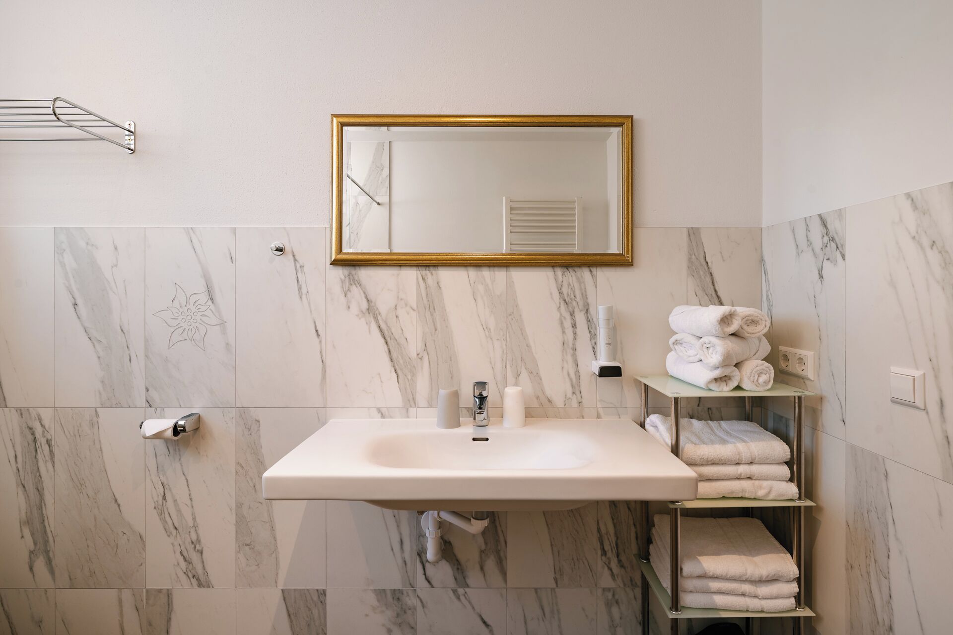 A bathroom with a marble wall, a sink, a mirror, and a towel rack.