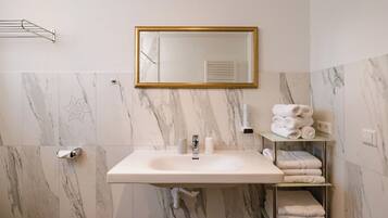 A bathroom with a marble wall, a sink, a mirror, and a towel rack.