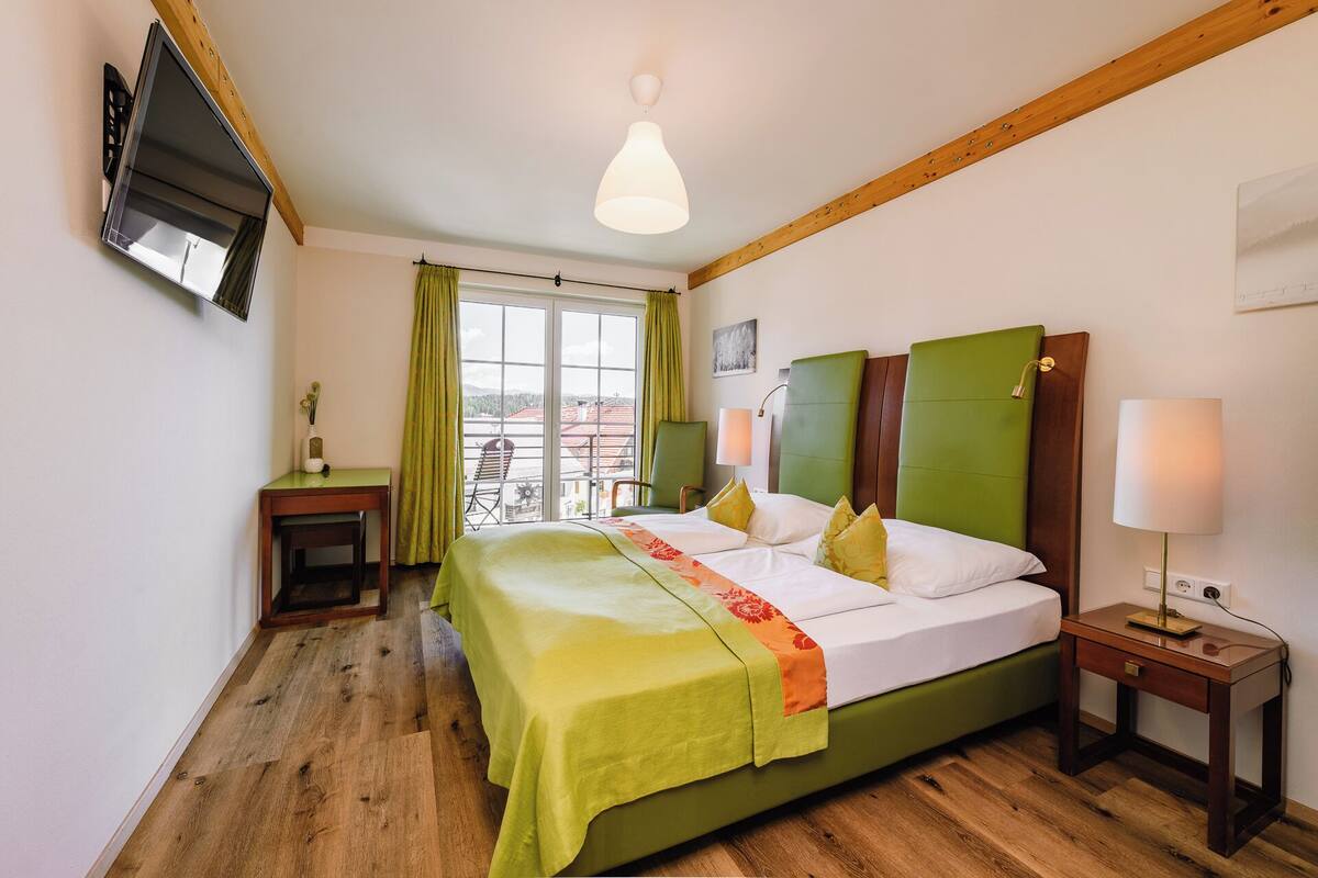 A hotel room with a bed, a desk, a chair, a TV, and a window with a view.