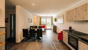 Een moderne keuken met houten kastjes, een inbouwoven en een eethoek met een tafel en stoelen.
