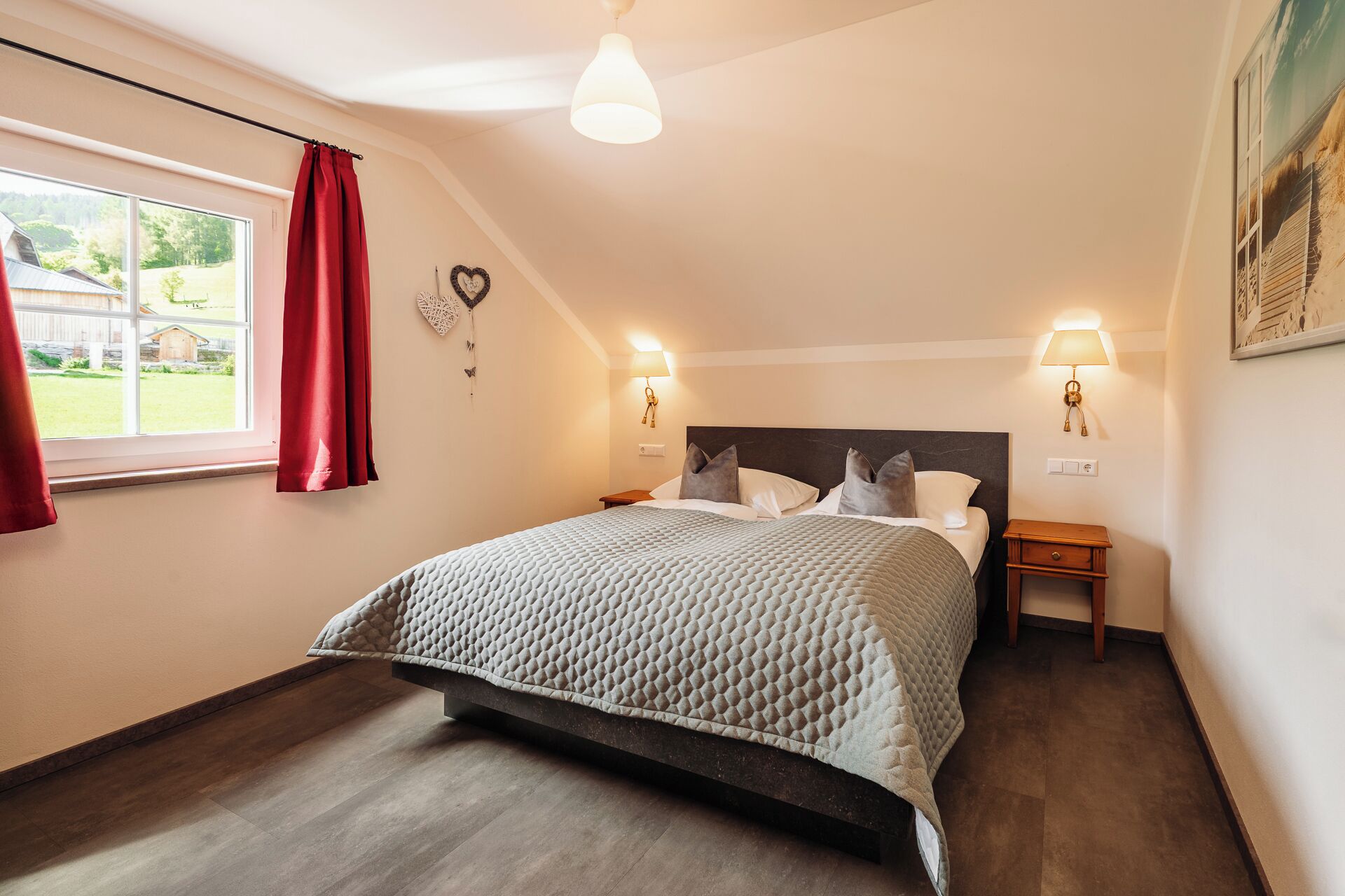 Een slaapkamer met een bed, twee nachtkastjes, een raam met gordijnen, een hartdecoratie aan de muur en een plafondlamp.