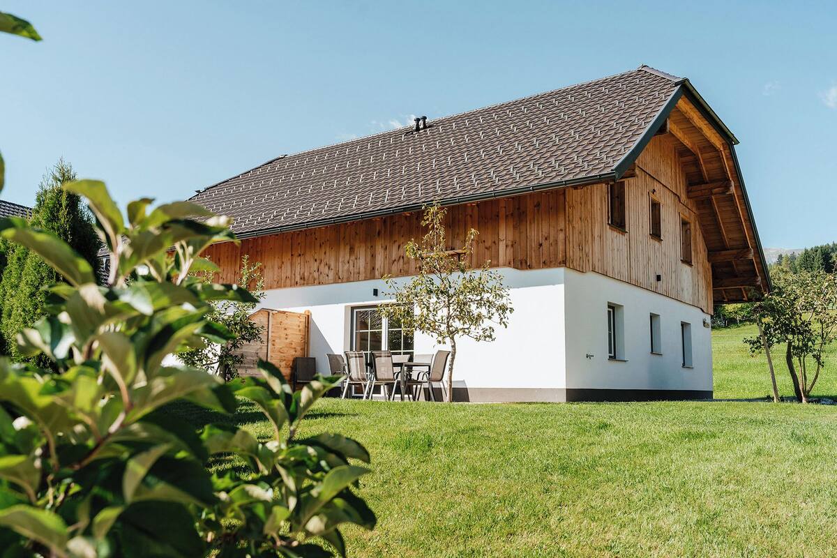 A two-story wooden house with a sloped roof, a front porch with a table and chairs, and a well-maintained lawn.