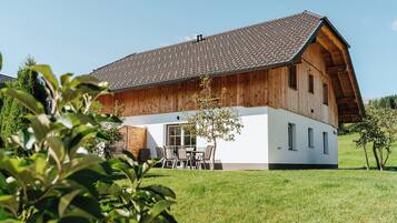 Ein zweistöckiges Holzhaus mit geneigtem Dach, einer Veranda mit Tisch und Stühlen und einem gepflegten Rasen.