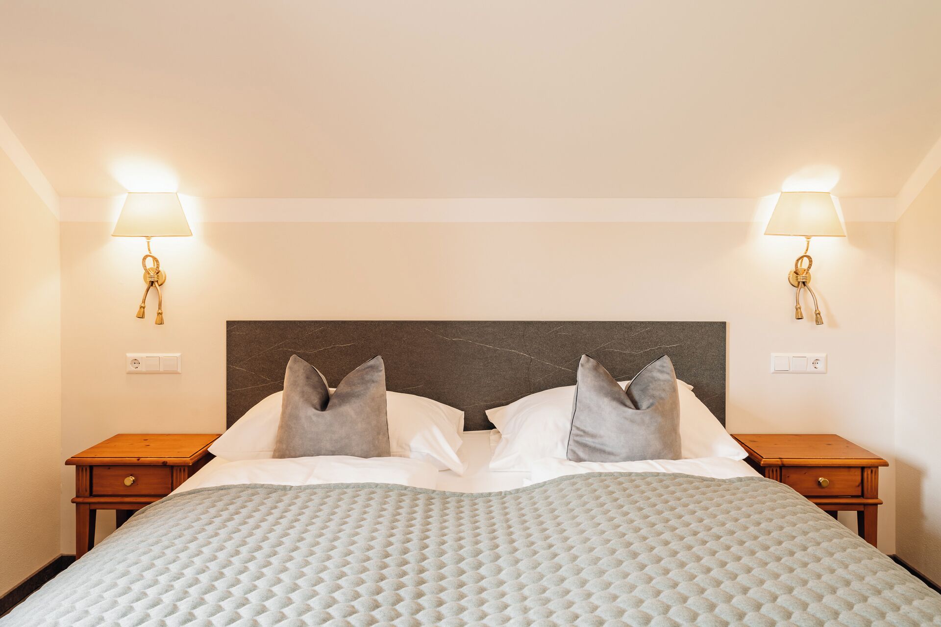 Habitación de hotel con una cama, dos mesitas de noche, dos lámparas de pared y un cabecero de mármol.