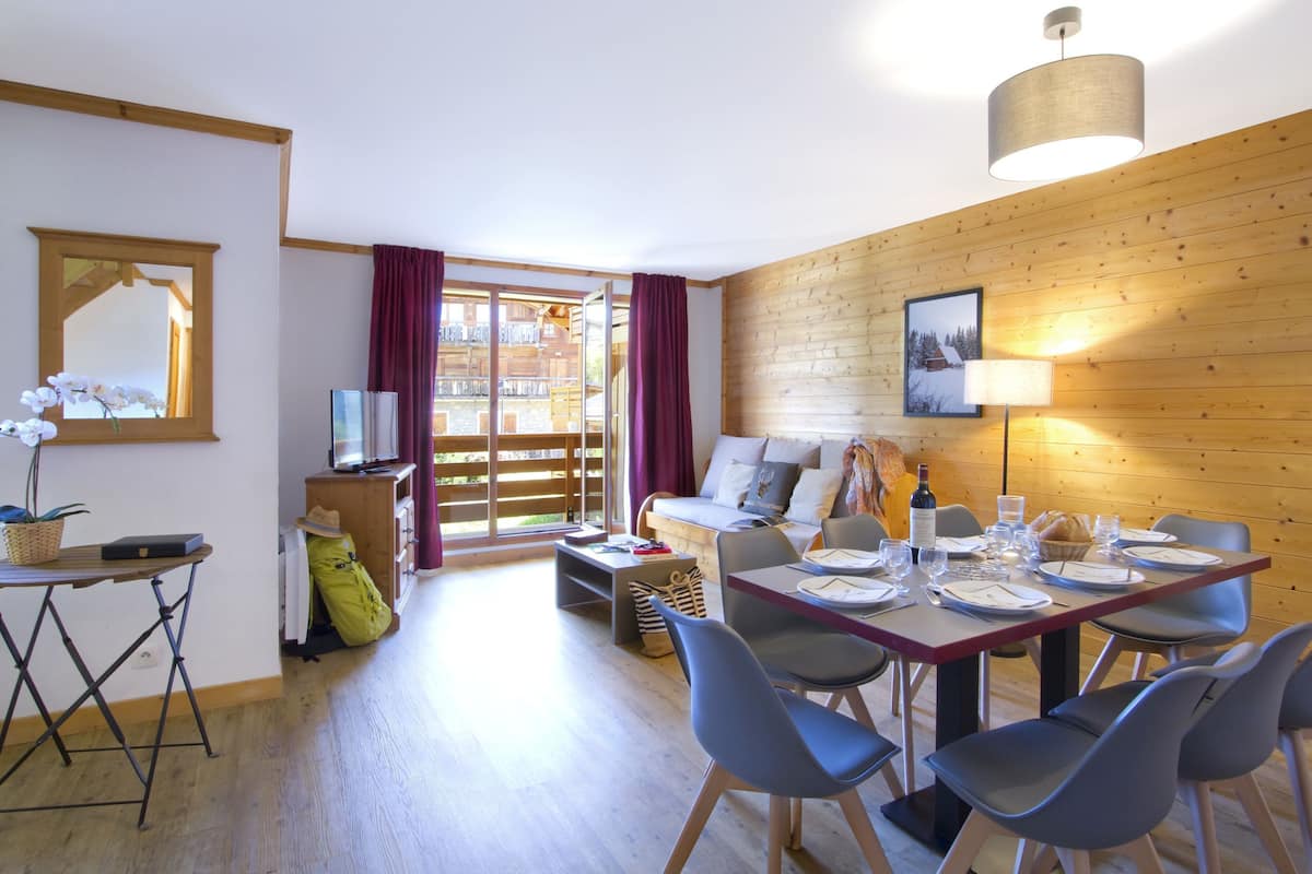 A modern room with a wooden wall, a dining table set for four, and a sofa.