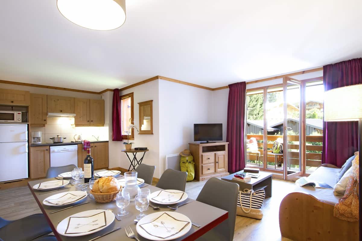 A well-lit room with a dining table set for four, a television, and a sofa.