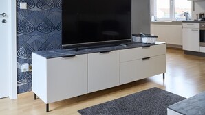 Een moderne keuken met een groot flatscreen-televisie op een marmeren aanrecht, witte kastjes en een decoratieve achterwand.