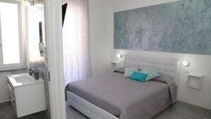 A bedroom with a bed, a nightstand, a bedside table, a window, and a bathroom. - B&B Mimì (Castelsardo)