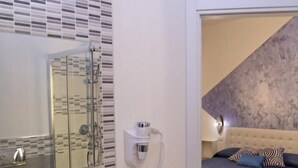 A modern bathroom with a large mirror, a white sink, and a shower. The room has a bed with a blue and patterned bedspread. - B&B Mimì (Castelsardo)