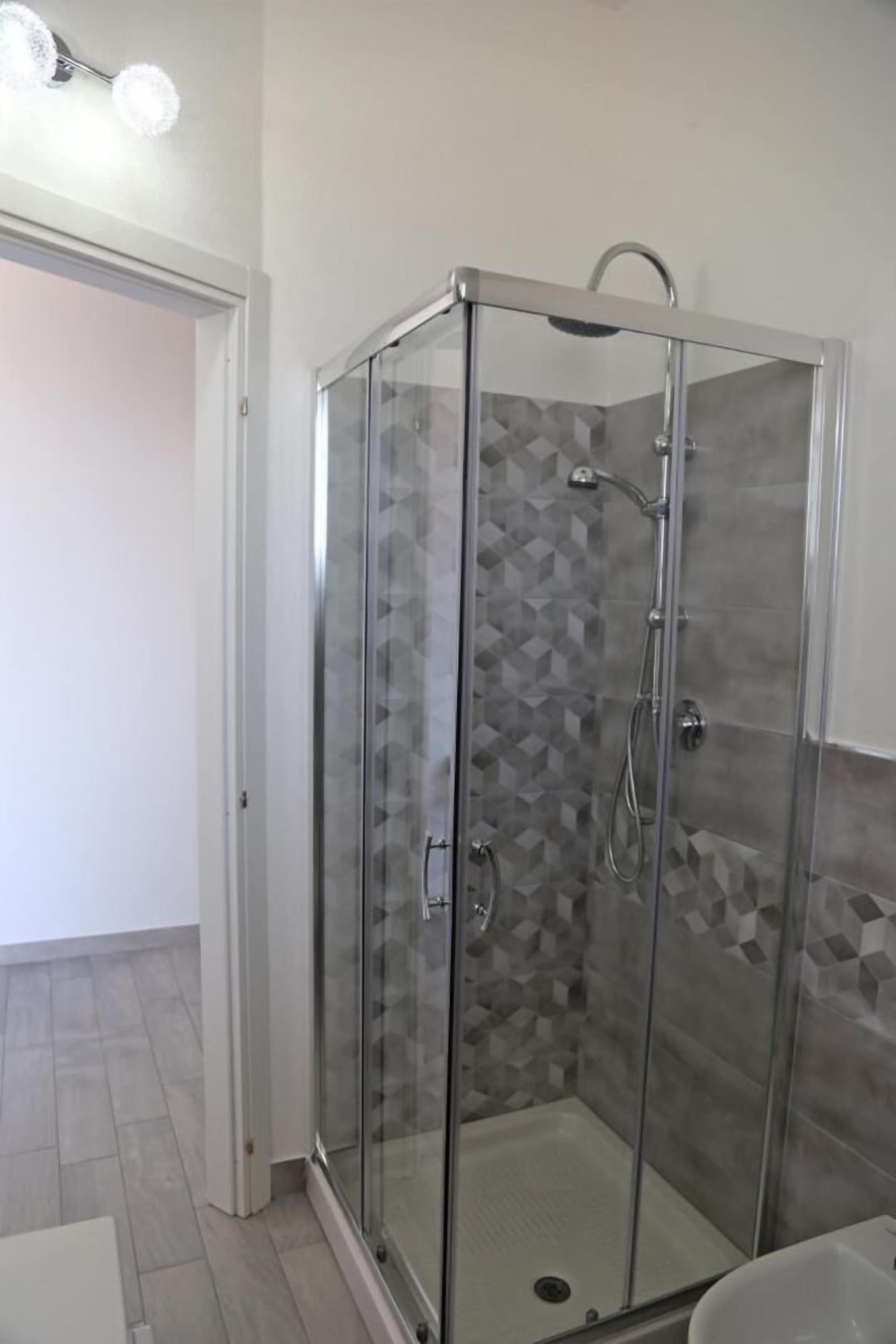 A glass-enclosed shower with a geometric tile wall, a visible drain, and a showerhead.