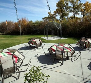 An outdoor patio area with tables and chairs, a swing set, and a gazebo. - Family Time Lodge: Indoor Playland, Theater Room, Game Room, 10 Master Suites (Garden City)