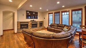 A living room with a stone fireplace, leather sectional sofa, and large windows with blinds.