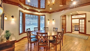 A dining area with a round table and chairs, wooden flooring, and a ceiling with wooden beams and recessed lighting.