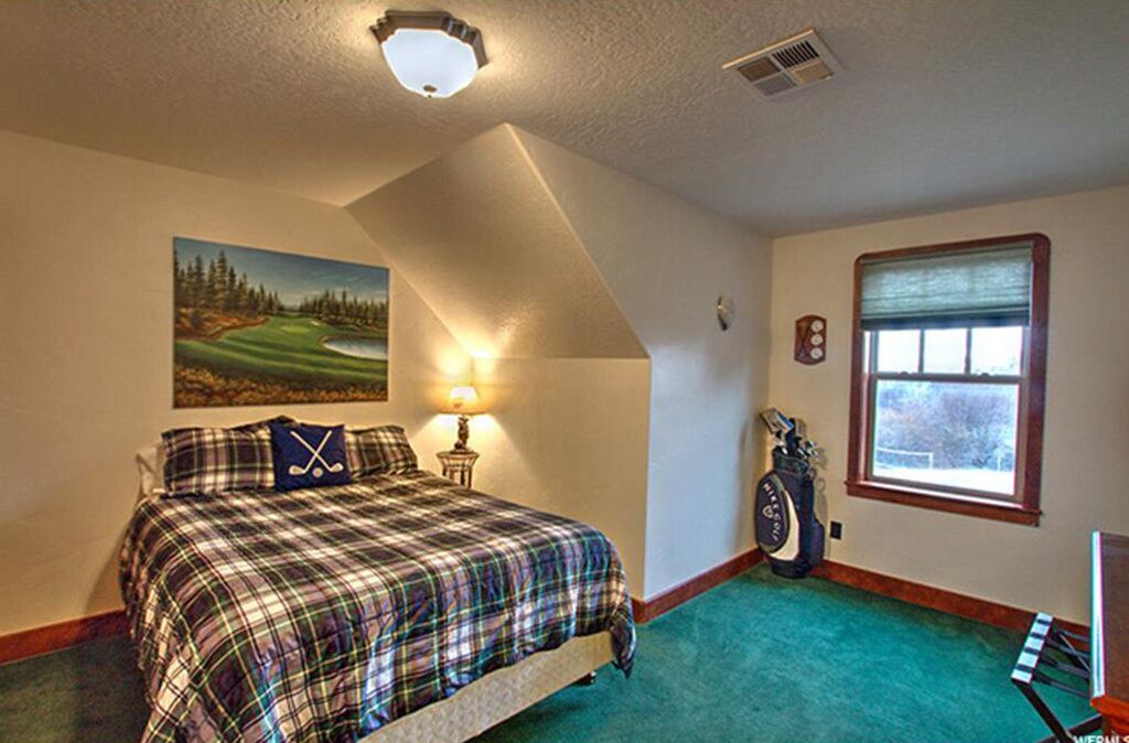 Ein Schlafzimmer mit Bett, Gemälde, Lampe, Fenster und einer Golfbag.