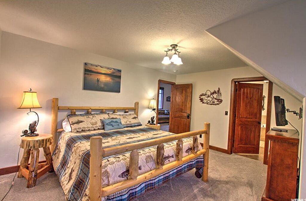 A bedroom with a wooden bed, two bedside lamps, a painting on the wall, and a ceiling fan.