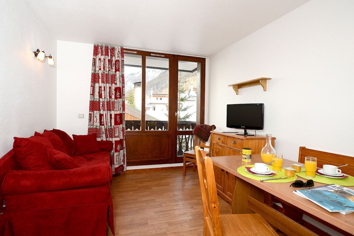 Uma sala de estar aconchegante com um sofá vermelho, uma mesa de jantar de madeira e uma televisão.