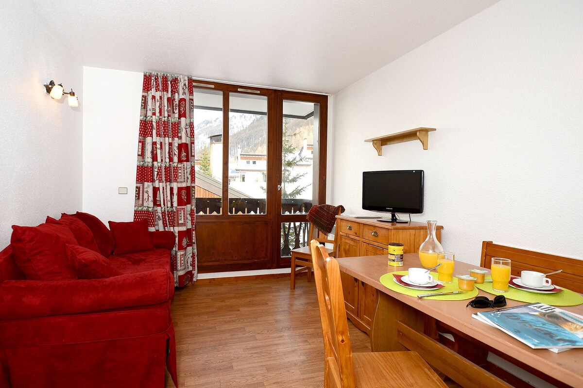 A cozy room with a red sofa, wooden dining table, breakfast setup, and a TV.