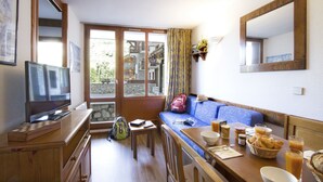Una habitación acogedora con un mueble de televisión de madera, un sofá, una mesa de comedor con productos para el desayuno y un gran ventanal con vistas a un edificio de piedra.