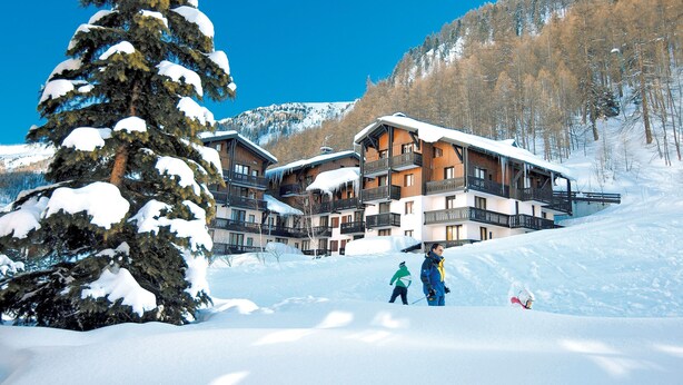 Una cabaña nevada con varios balcones y una pista de esquí al fondo.