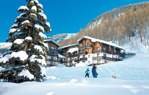 A snow-covered lodge with multiple balconies and a ski slope in the background.