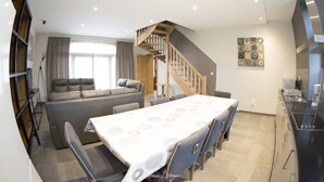 Une cuisine moderne dotée d’une cuisinière intégrée, un coin repas avec une table et des chaises, un escalier menant à une mezzanine, et un espace de vie avec un canapé et une table basse.