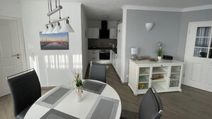 A modern kitchen with white cabinets, a dining area with a round table and chairs, and a white cabinet with glass doors. - (311/2) 3- room apartment Ostseeallee - (300) Pier Kühlungsborn (Kühlungsborn)
