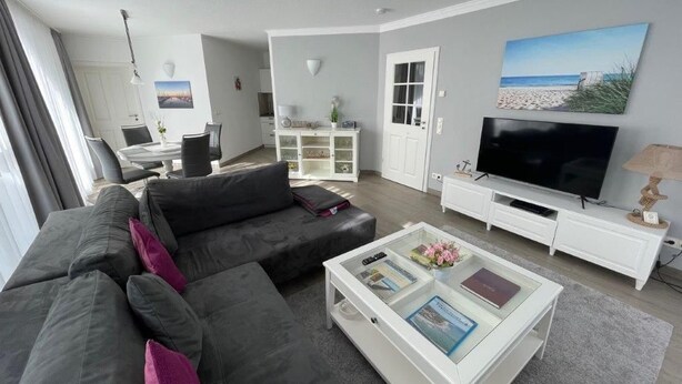 A modern living room with a grey sofa, a glass coffee table, a flat-screen TV, and a painting of a beach scene. - (311/2) 3- room apartment Ostseeallee - (300) Pier Kühlungsborn (Kühlungsborn)