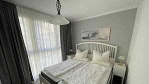 A bedroom with a white bed, a nightstand, a lamp, and a painting on the wall. - (311/2) 3- room apartment Ostseeallee - (300) Pier Kühlungsborn (Kühlungsborn)
