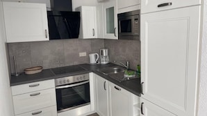 A modern kitchen with white cabinets, a built-in oven, a microwave, and a coffee maker. - (311/2) 3- room apartment Ostseeallee - (300) Pier Kühlungsborn (Kühlungsborn)
