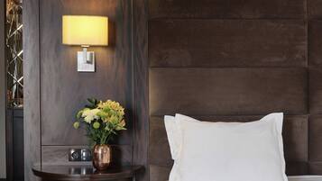 A hotel room with a bed, a bedside lamp, a vase with flowers, and a nightstand.