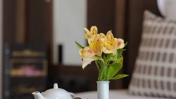 A tray with croissants, grapes, and pears on a table, a white teapot, and a vase with flowers in a hotel room.