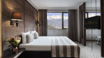Habitación de hotel con una cama grande, televisión de pantalla plana, un piano y vistas a la montaña.
