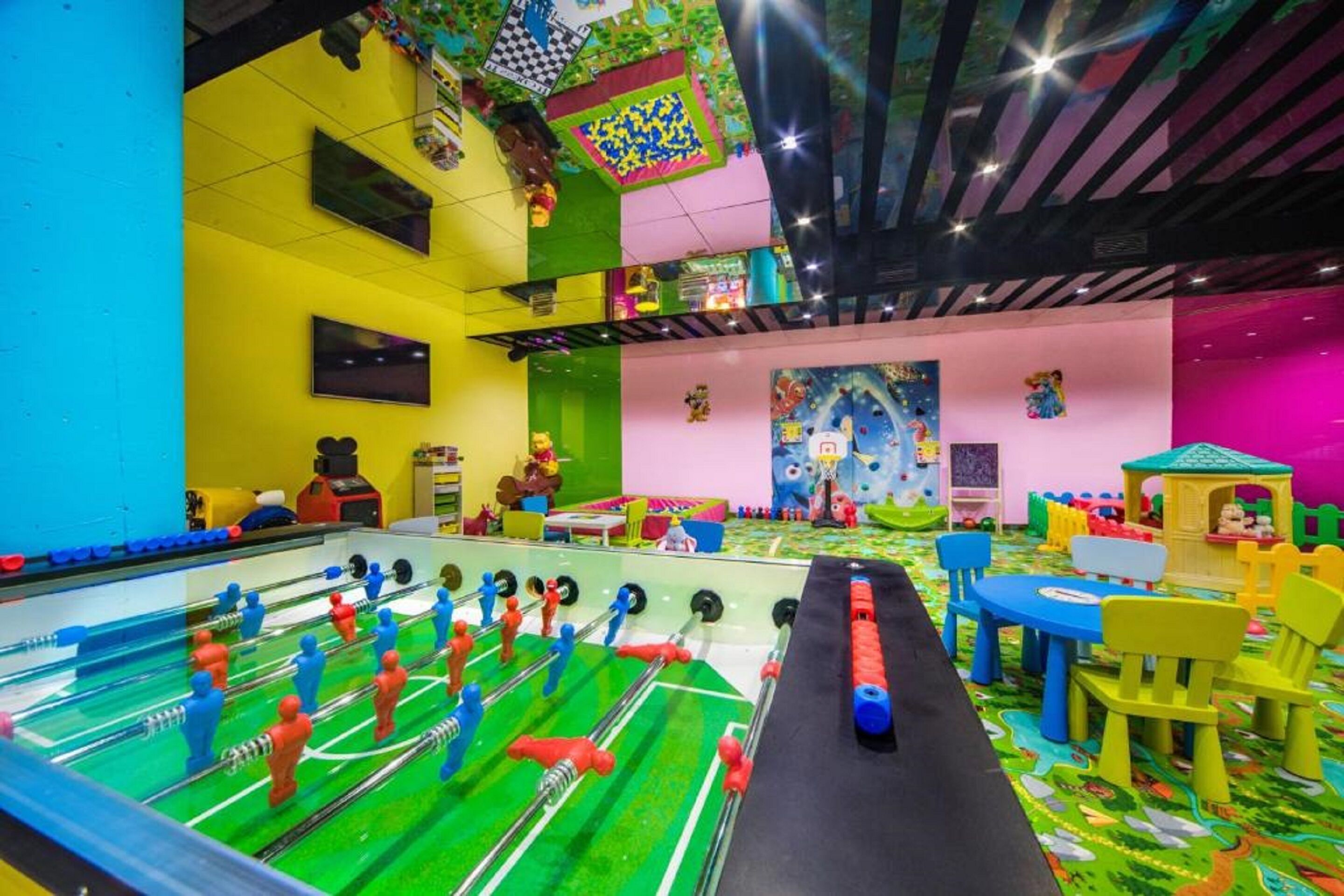 Un área de juegos interior muy colorida con una mesa de fútbol de mesa, estructuras de juego coloridas y un mural en la pared.