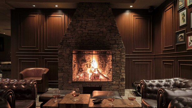 Ein gemütlicher Lounge-Bereich mit Ledersofas, einem Kamin aus Stein und gerahmten Bildern an der Wand.